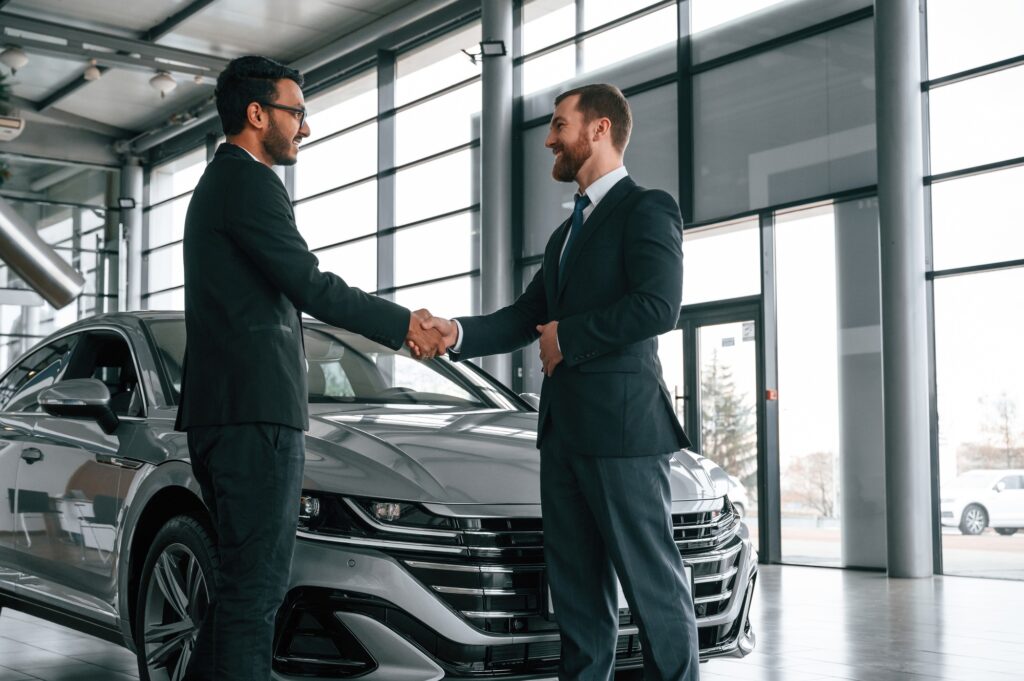 Doing handshake. Man is consulting the customer in the car showroom